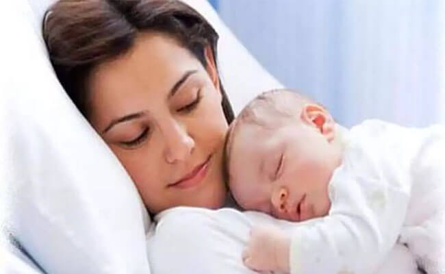 Portrait picture a happy woman lying in bed, holding her sleeping baby.